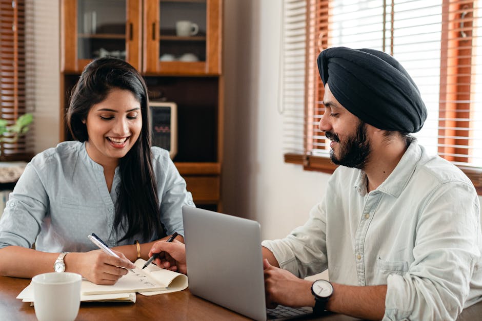 Young positive Indian man and woman sitting together at table with laptop and cup of coffee and doing homework online